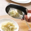 Garlic press with black handle on a wooden table.