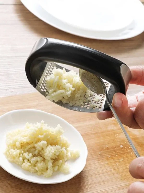 Garlic press with black handle on a wooden table.